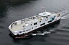 En hvit katamaranferje seiler på mørkt vann sett ovenfra.