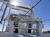 Dekk på et stort fiskefartøy med vinsjer, master, tauverk og metallkonstruksjoner i sollys.
