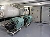 Et lyst maskinrom med to store motorer, hvite rør og elektriske kontrollskap langs veggen.