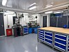 Lyst verkstedrom med arbeidsbenker, verktøy, skap og industrielle installasjoner.