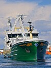 Et stort grønt og hvitt fiskefartøy ligger ved kai med dekkskraner og bro synlig forfra.