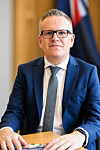 En mann i blå dress sitter ved et bord foran et norsk flagg.