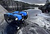 Blå fjernstyrt undervannsrobot på stein ved vann med skog og fjell i bakgrunnen.