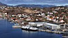 Kystby med havn, flere fartøy, kaianlegg og store verftsbygninger sett fra luften.