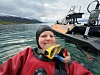 Dykker i rødt utstyr flyter ved siden av en arbeidsbåt i en fjord.