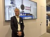 Mann i dress står foran en skjerm med illustrasjon av industrielt utstyr på en messe.