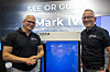 To personer i svarte Decca-skjorter står ved en blå messepresentasjon med teksten Mark IV.