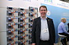 Smilende mann i dress står ved siden av et modulbasert batterisystem på en messe.