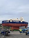 Blått og rødt Reach Subsea-fartøy på land ved et verft, med arbeidere og utstyr i forgrunnen.