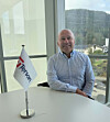 Smilende mann sitter ved et bord foran et vindu med en Tersan-logo på et lite flagg.