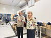 To ansatte i et lyst produksjonslokale med maskiner og arbeidsbenker.