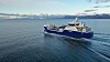 Blå og hvit arbeidsbåt på fjorden med fjellandskap i bakgrunnen.